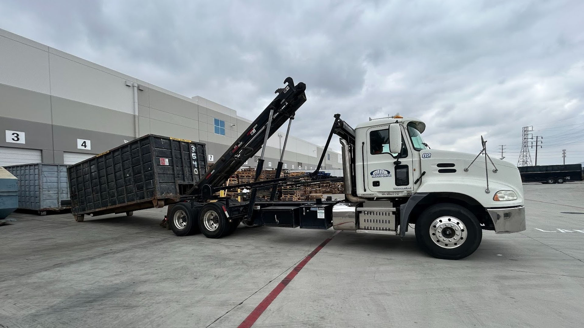 A JD Transport roll-off truck setting a dumpster at a commercial loading dock