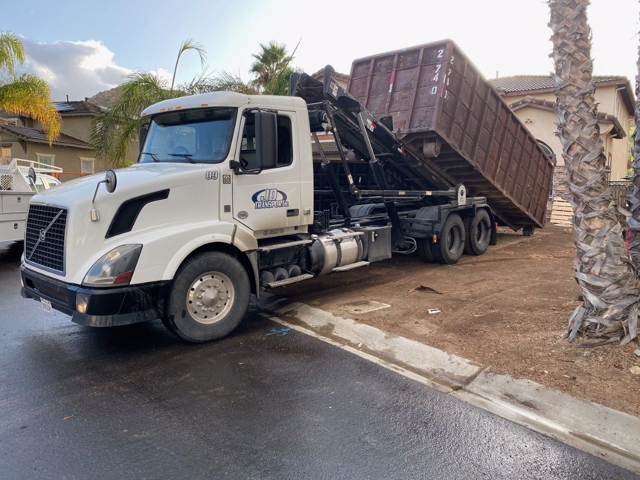 JD Roll Off Dumpsters Volvo truck setting a 20 yard dumpster in a Moreno Valley driveway