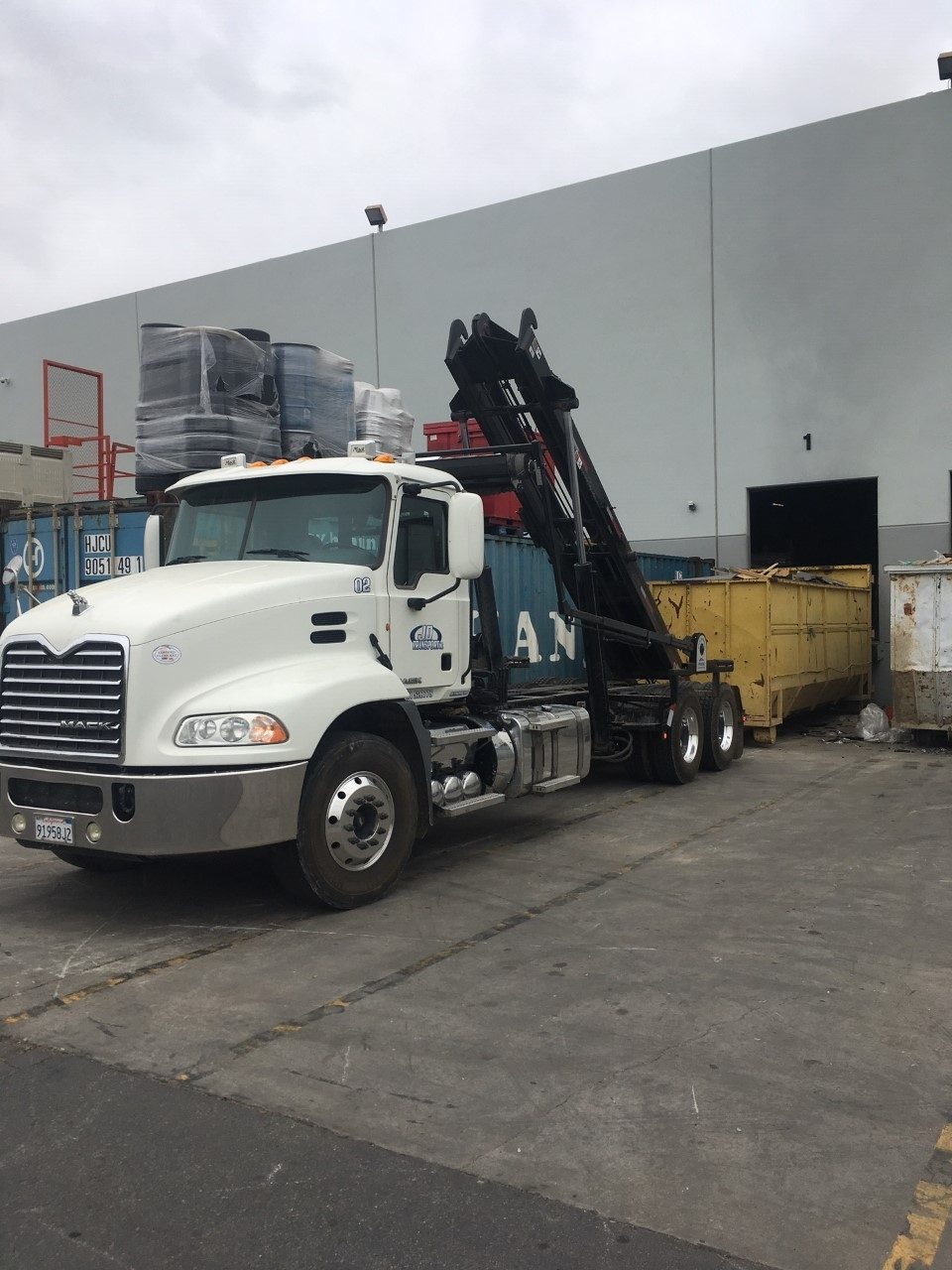 JD Transport roll-off truck swapping a commercial dumpster at an Inland Empire warehouse dock