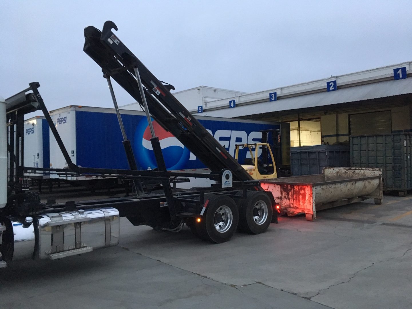 JD Roll Off Dumpsters truck backing an empty container to a distribution center loading dock