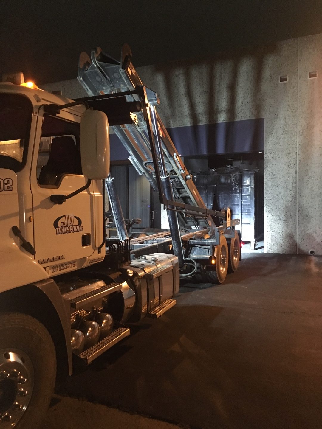 JD Transport roll-off truck placing a dumpster inside a warehouse at night