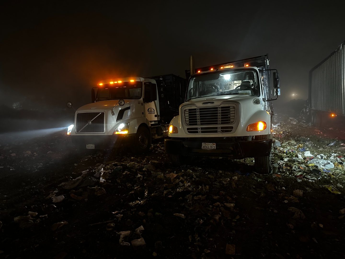 Two JD Transport roll-off trucks unloading at a Southern California landfill at night